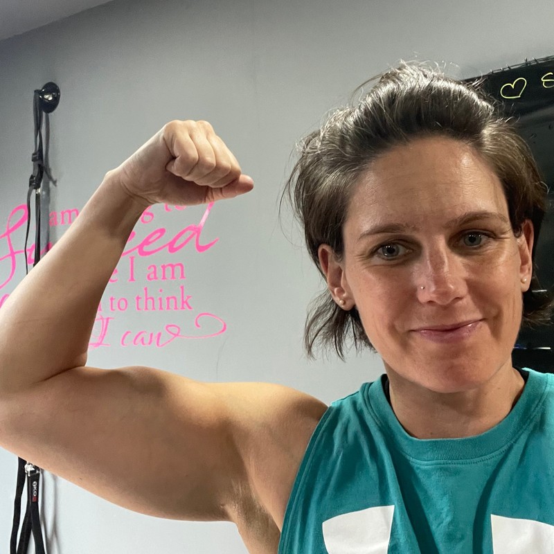 Hannah, smiling and flexing her arm in the gym